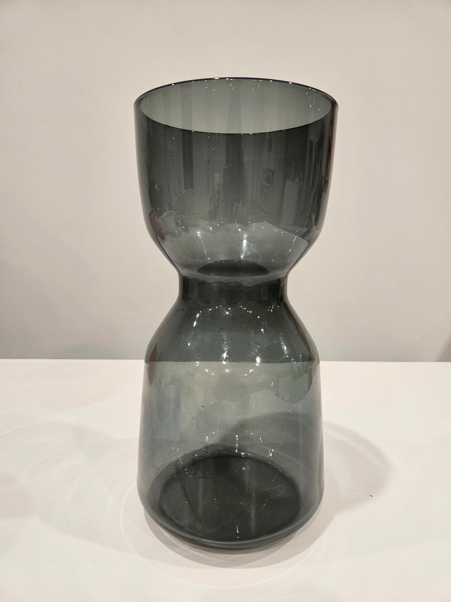Dark glass hourglass-shaped object on a white surface with a light gray background
