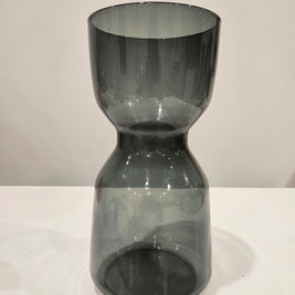 Dark glass hourglass-shaped object on a white surface with a light gray background