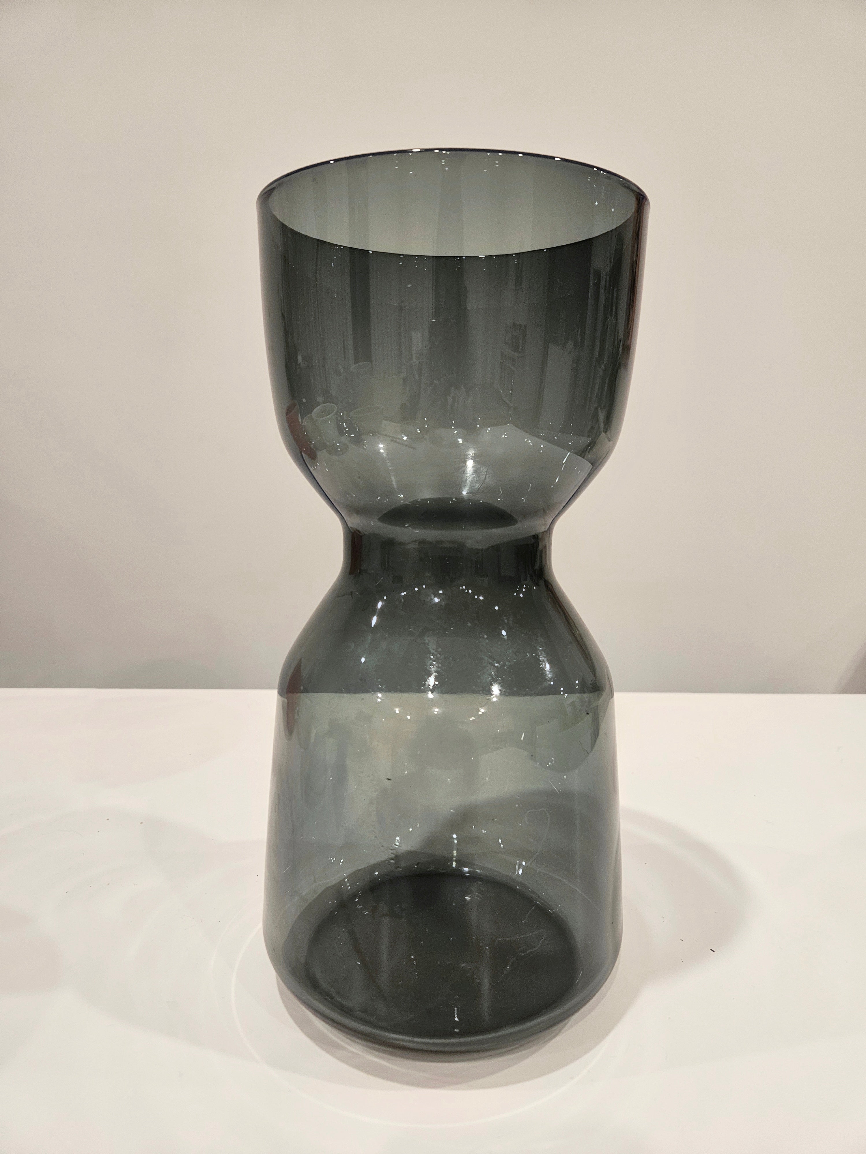 Dark glass hourglass-shaped object on a white surface with a light gray background