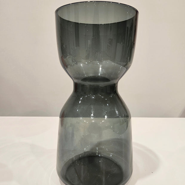 Dark glass hourglass-shaped object on a white surface with a light gray background