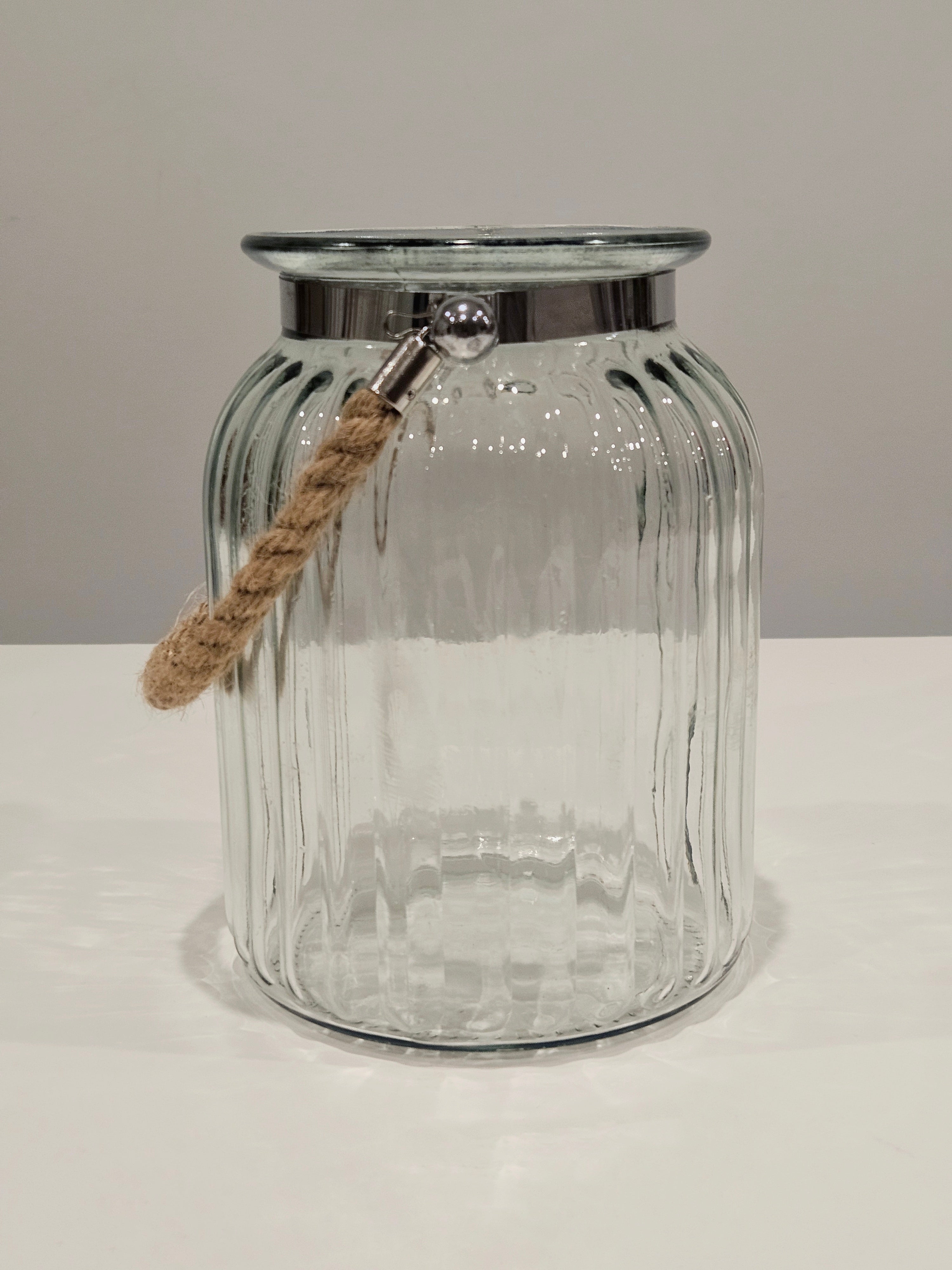 Clear glass jar with a silver lip and rope handle on a white surface.
