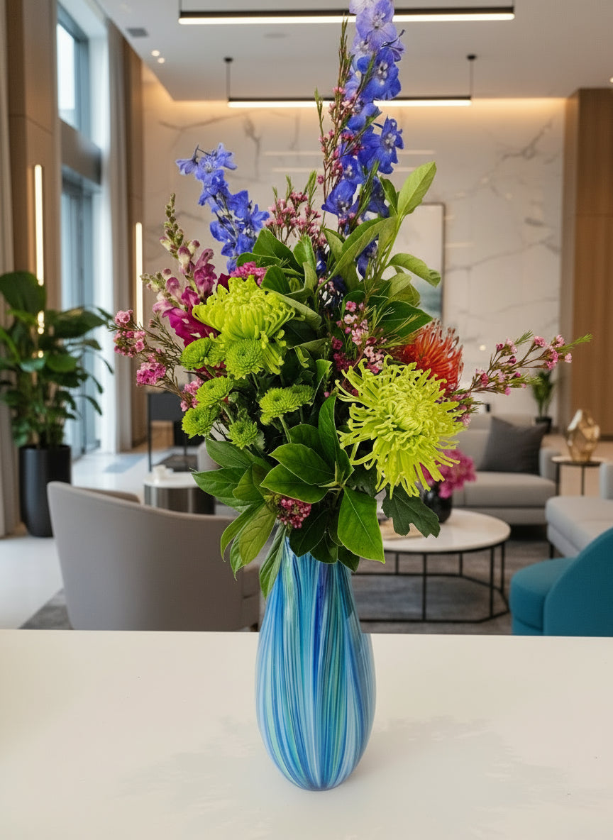 Colourful bouquet of flowers in a blue and white striped vase on a table with a blue cushioned chair in the background.