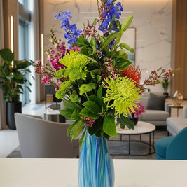 Colourful bouquet of flowers in a blue and white striped vase on a table with a blue cushioned chair in the background.