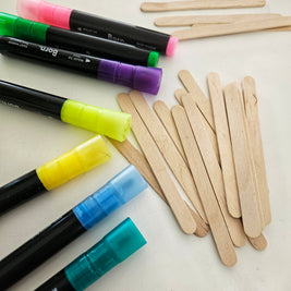 Colourful paint markers and wooden popsicle sticks on a white surface