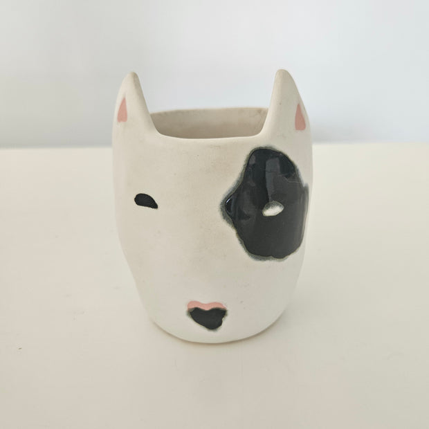 Ceramic vase shaped like a dog's face with black eyes and nose on a white background