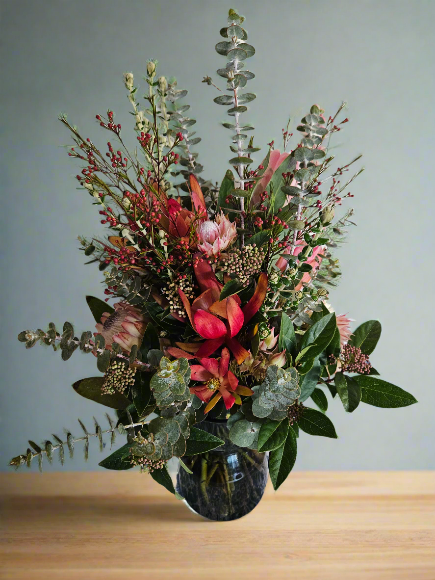 Floral arrangement in a charcoal vase on a wooden surface with a grey background