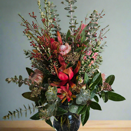 Floral arrangement in a charcoal vase on a wooden surface with a grey background