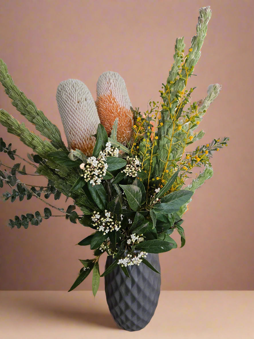 Bouquet of Australian native flowers in a textured grey vase against a beige background