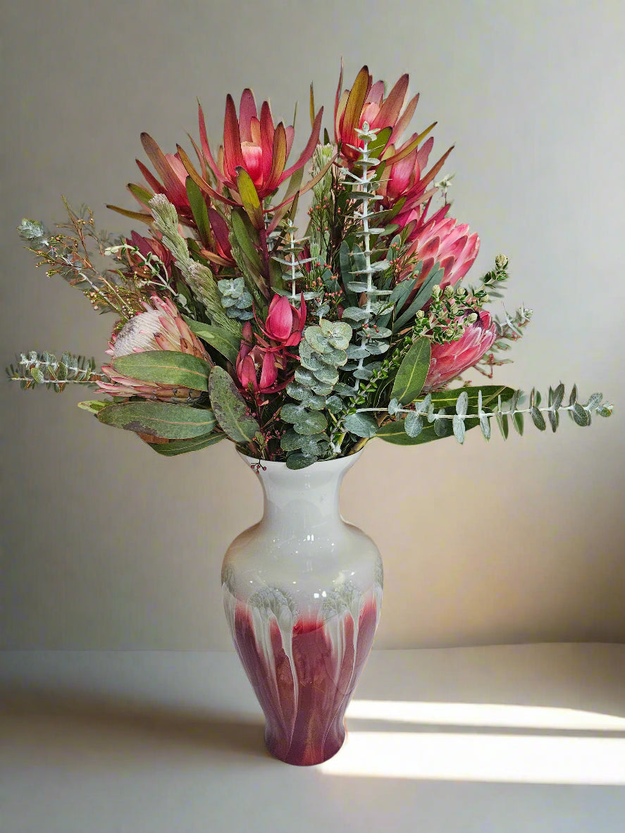 Bouquet of red and green flowers in a white and red drip vase on a light background