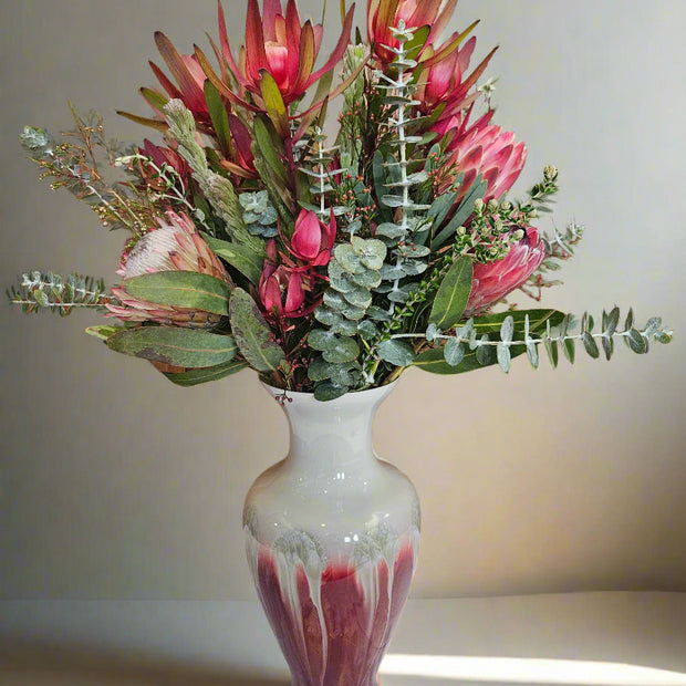 Bouquet of red and green flowers in a white and red drip vase on a light background