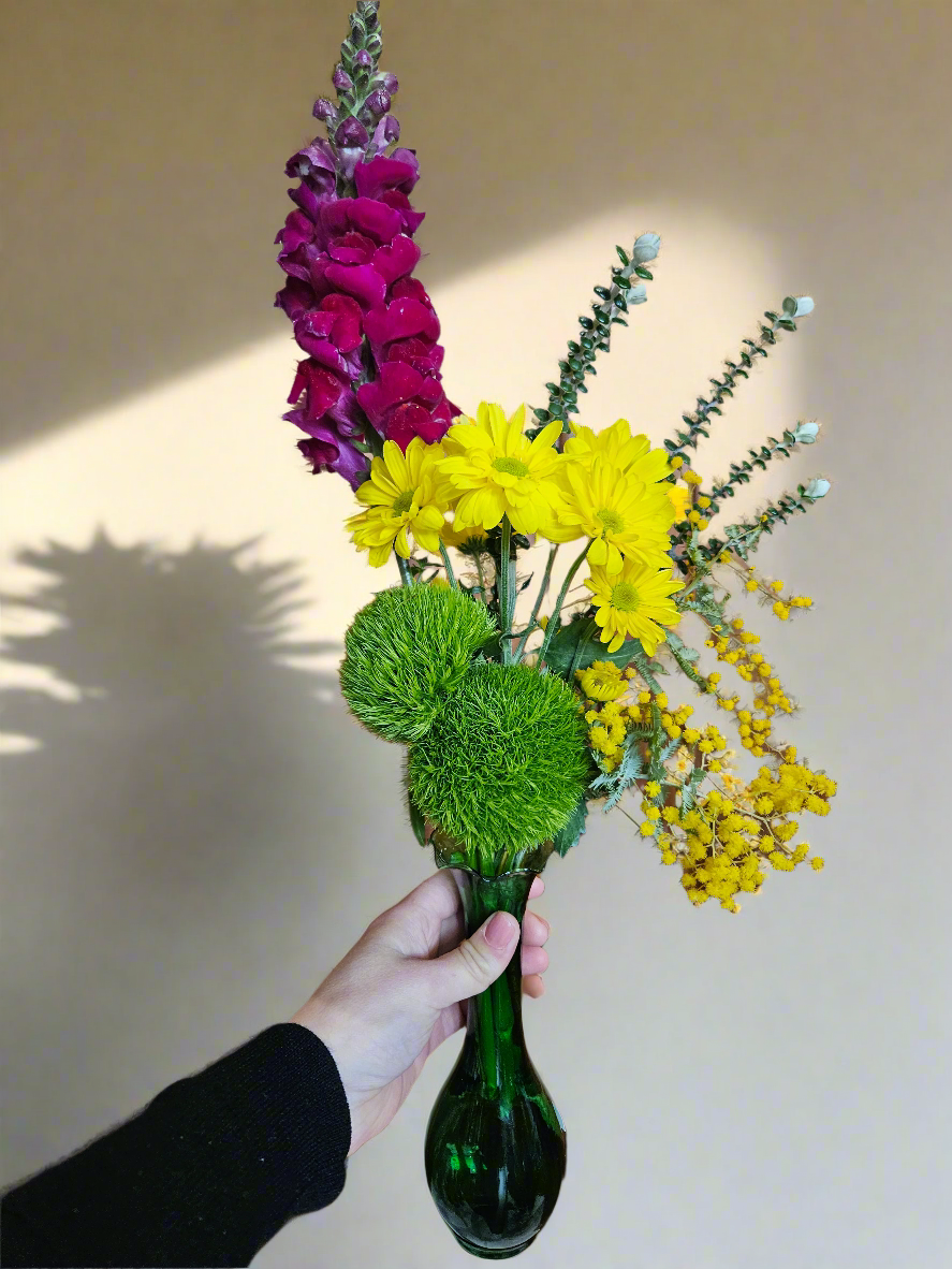 Bouquet of flowers in a green vase held by a hand against a neutral background