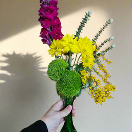 Bouquet of flowers in a green vase held by a hand against a neutral background