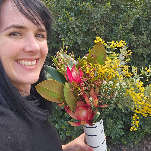Person holding a bouquet of flowers with greenery in the background