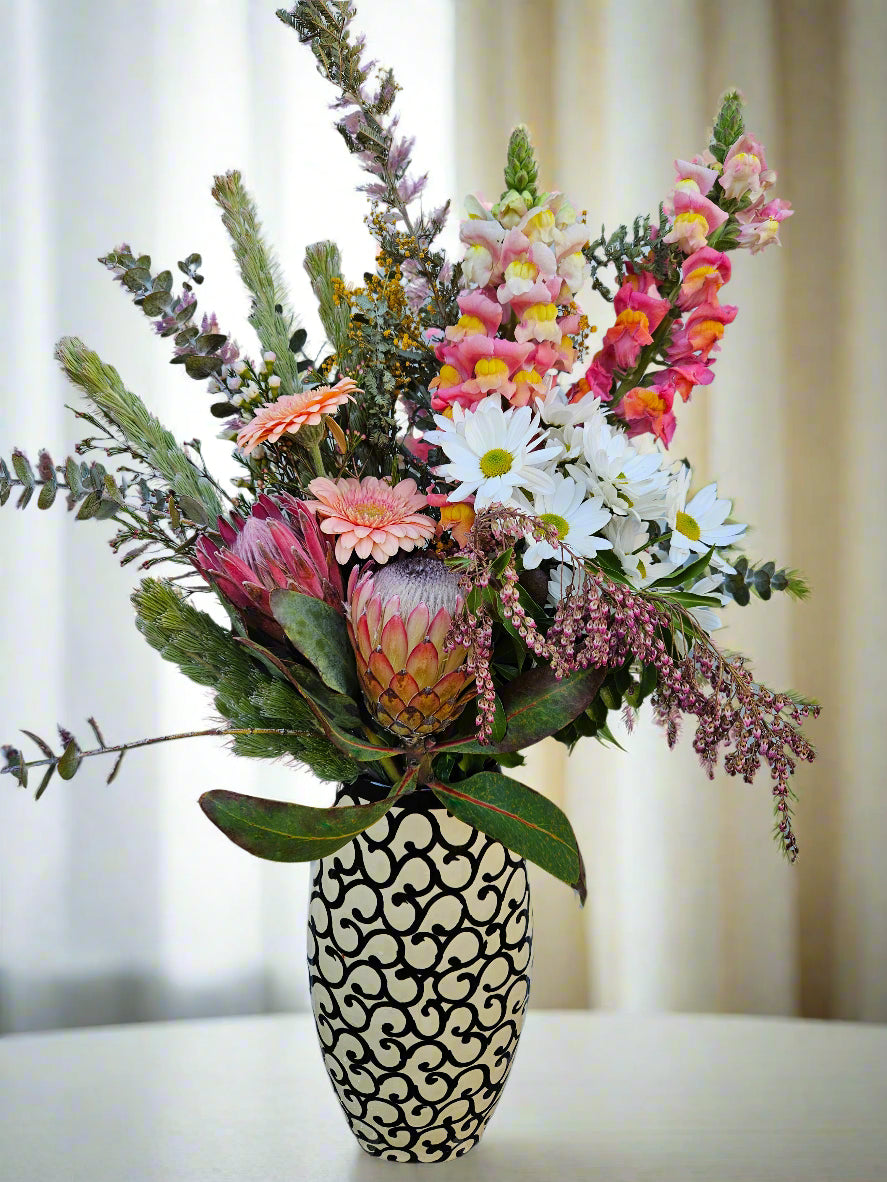 Bouquet of flowers in a decorative black and white vase on a white surface with a blurred background