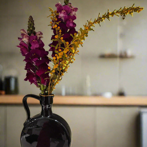 Black vase with purple and yellow flowers on a wooden table in a kitchen setting