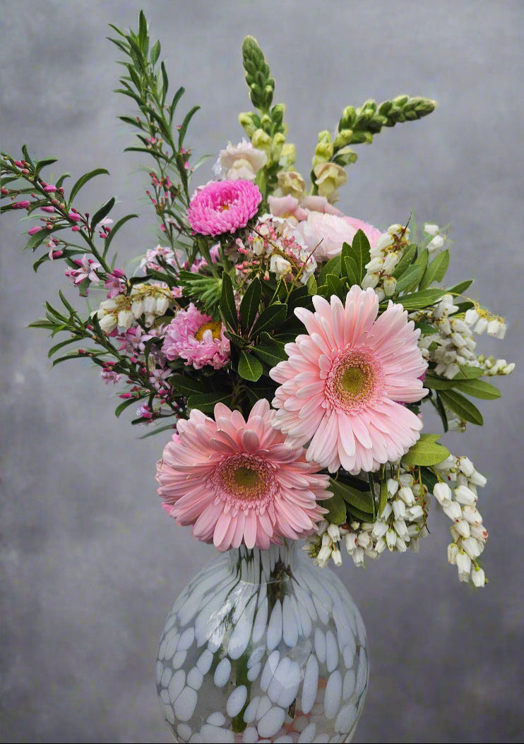 Bouquet of pink and white flowers in a spotted white vase against a grey background