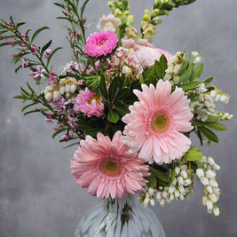 Bouquet of pink and white flowers in a spotted white vase against a grey background