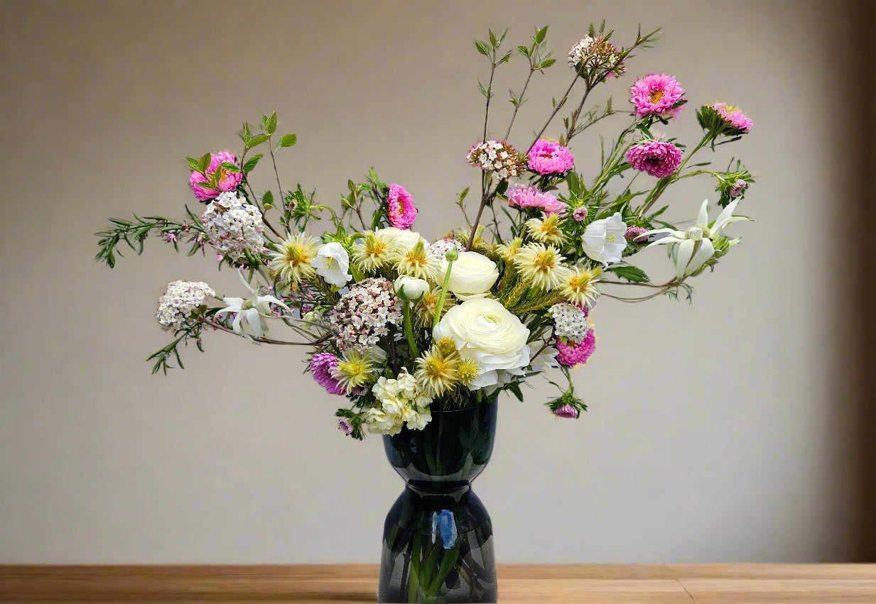 Bouquet of flowers in a dark vase on a wooden surface with a neutral background
