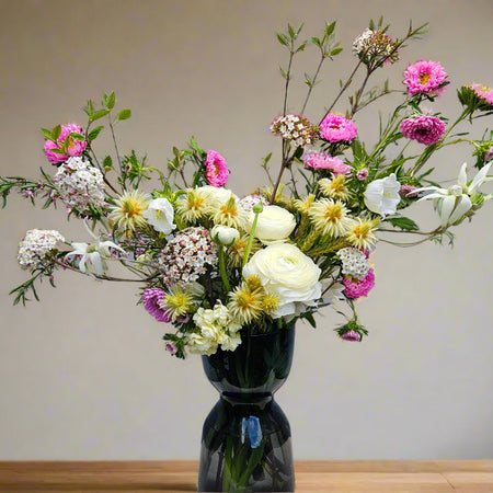 Bouquet of flowers in a dark vase on a wooden surface with a neutral background