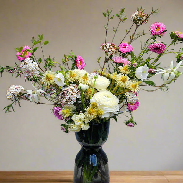 Bouquet of flowers in a dark vase on a wooden surface with a neutral background