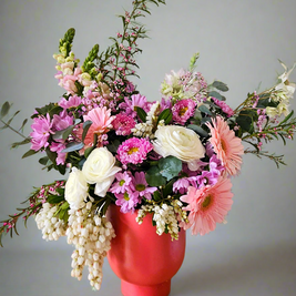 Colourful flower arrangement in a peach pot on a grey background