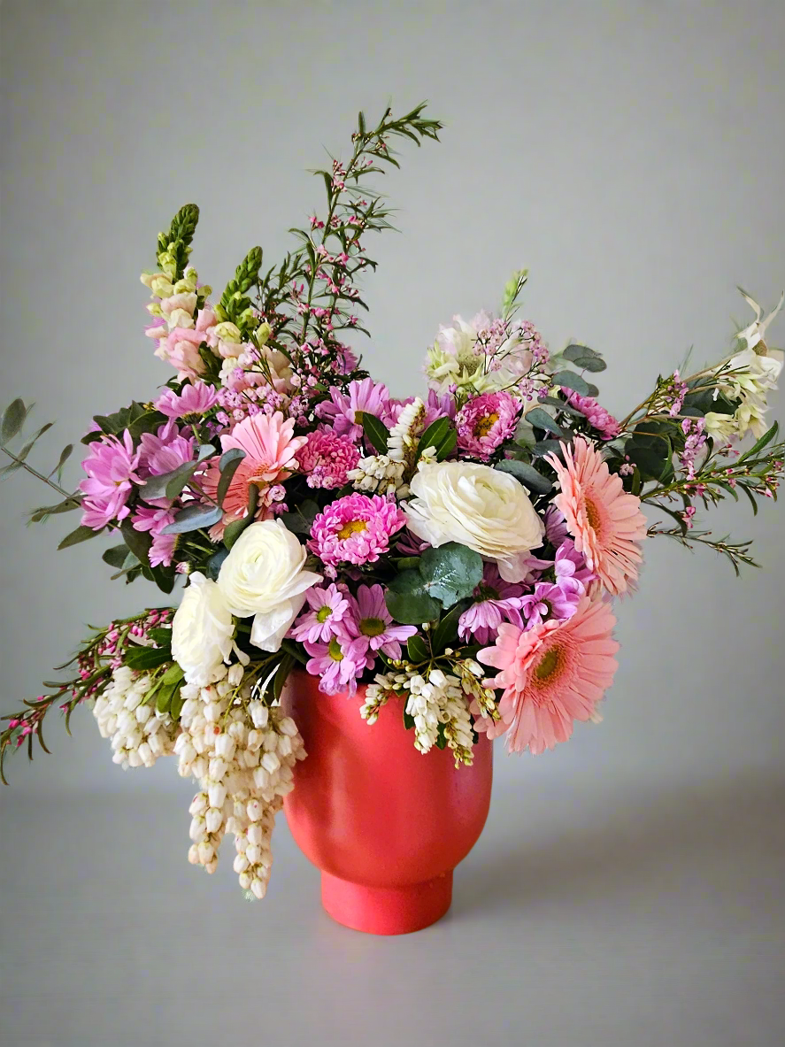 Colourful flower arrangement in a peach pot on a grey background