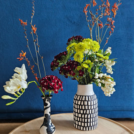 Two flower arrangements in black and white vases against a blue background