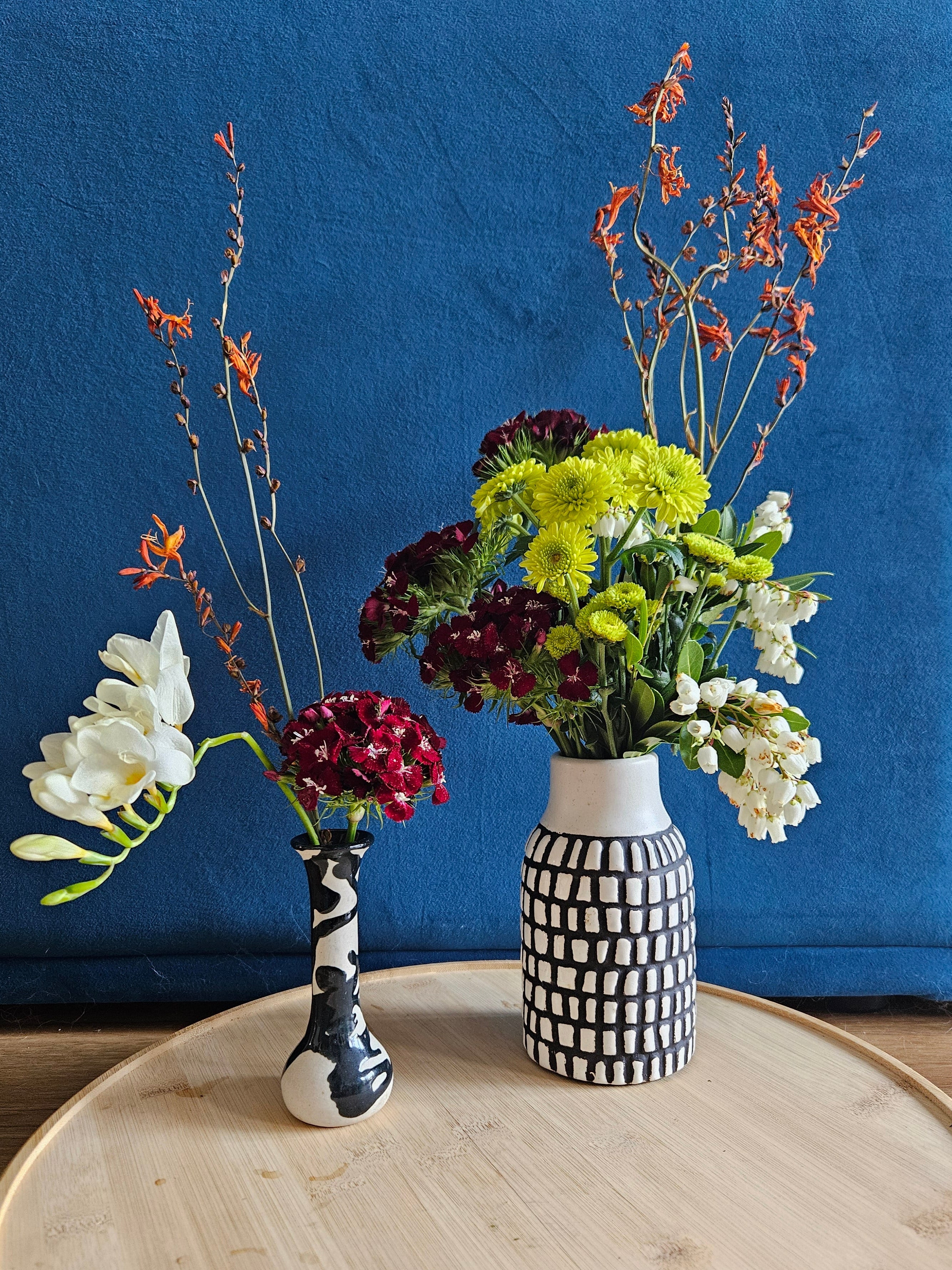 Two flower arrangements in black and white vases against a blue background
