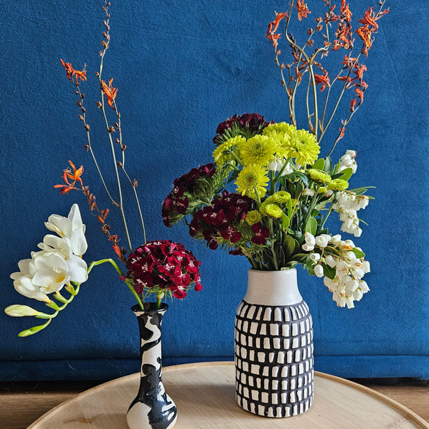 Two flower arrangements in black and white vases against a blue background