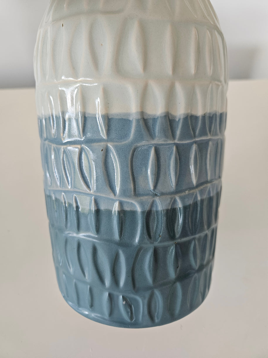 Cylindrical blue and white ceramic vase with textured pattern on a white background