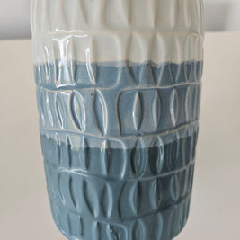 Cylindrical blue and white ceramic vase with textured pattern on a white background