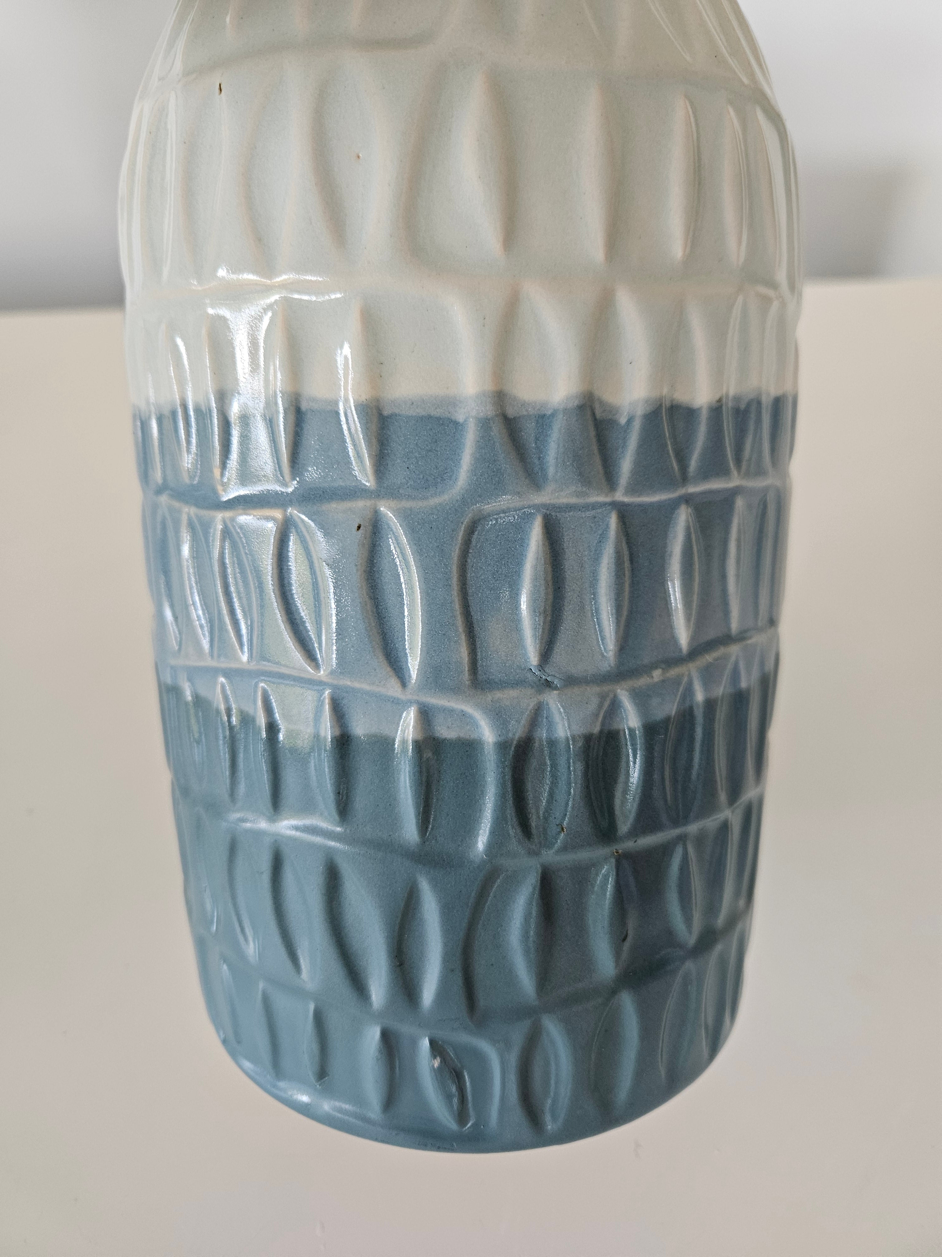 Cylindrical blue and white ceramic vase with textured pattern on a white background