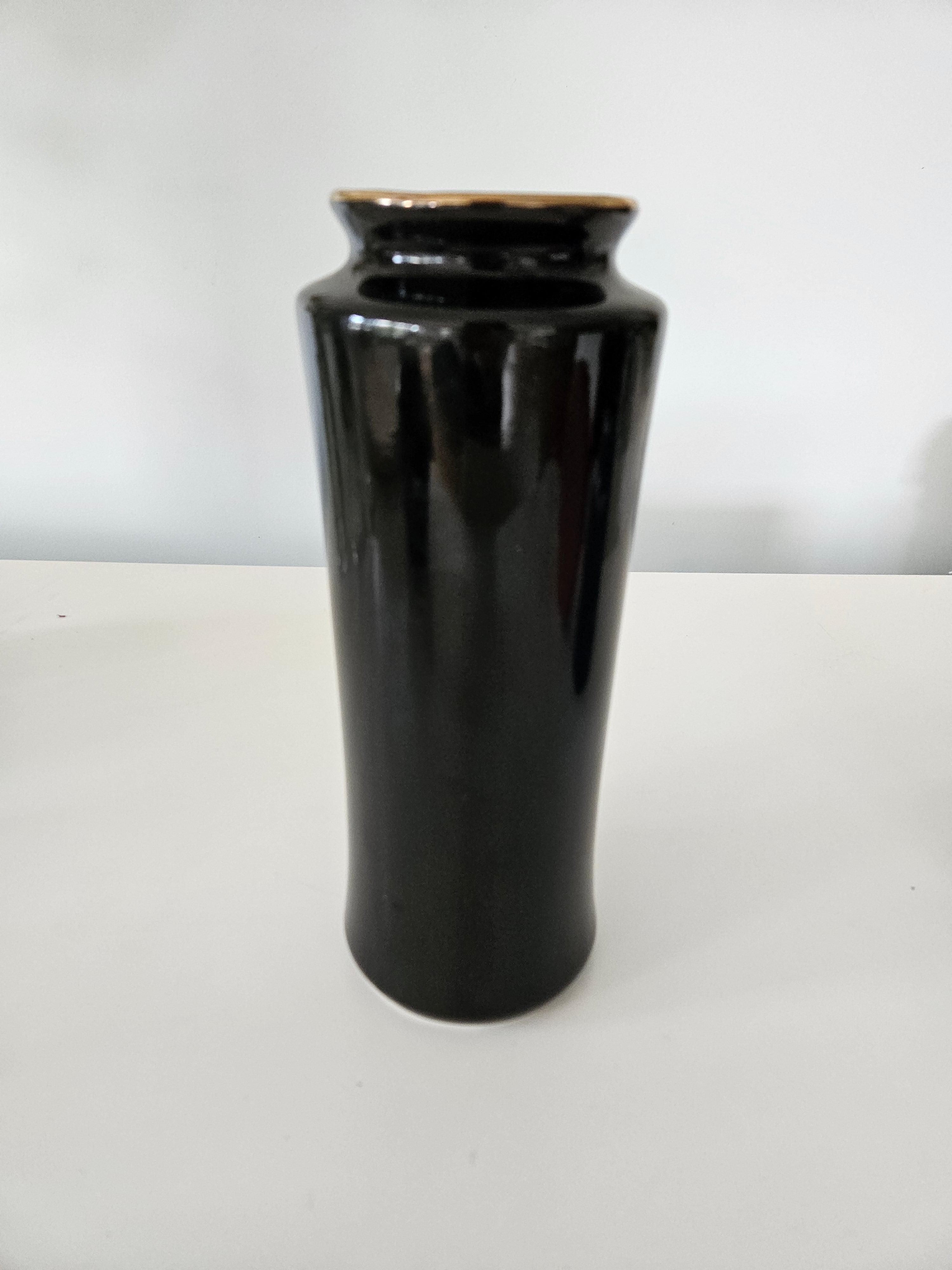 Back of a black ceramic vase with a gold rim on a white background