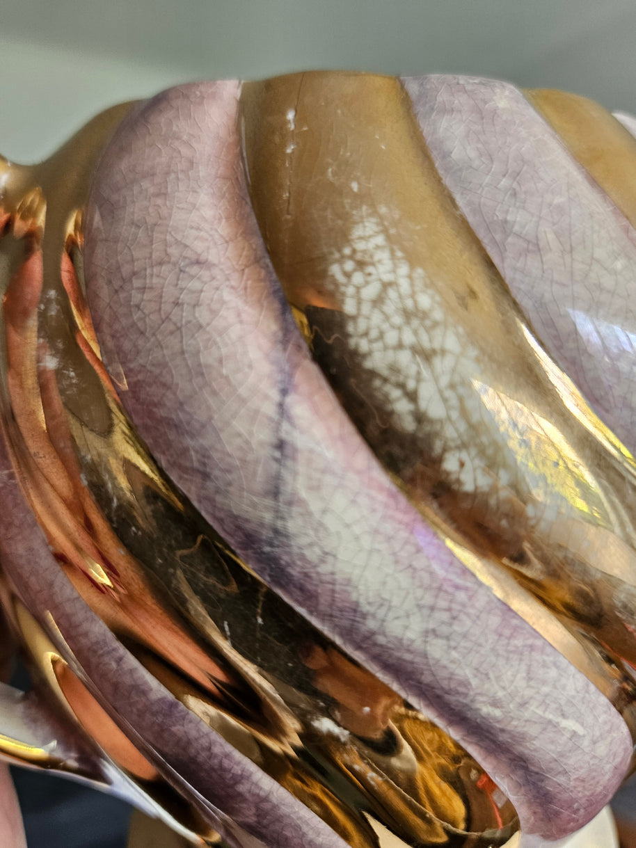 Close-up of a chips and crazing on a gold and purple coloured vase on a neutral background