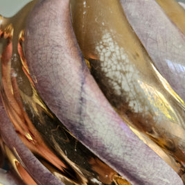 Close-up of a chips and crazing on a gold and purple coloured vase on a neutral background