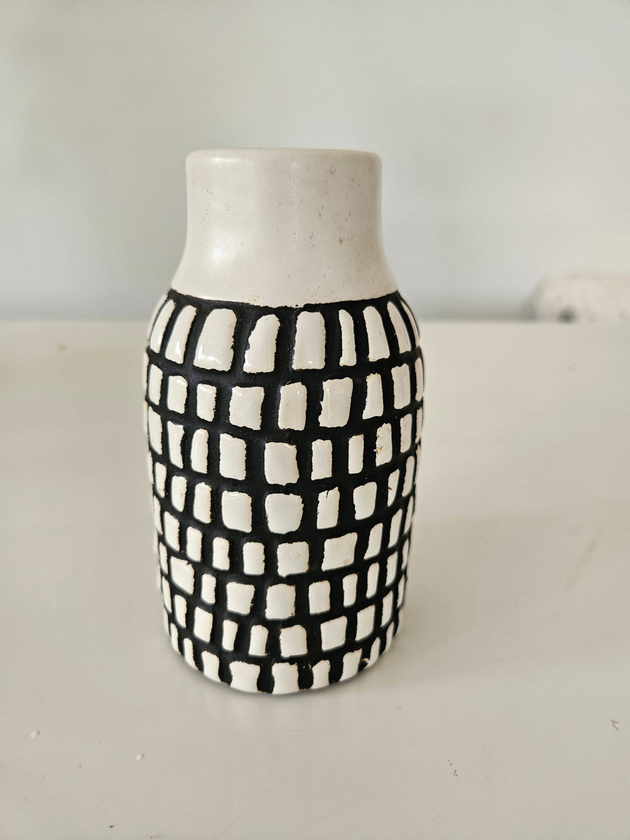 Cylindrical ceramic vase with black and white checkered pattern on a plain background