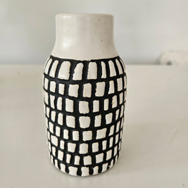 Cylindrical ceramic vase with black and white checkered pattern on a plain background