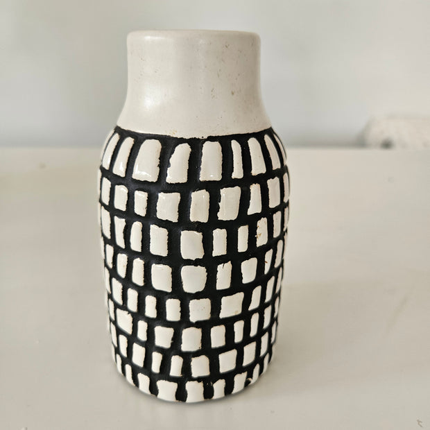 Cylindrical ceramic vase with black and white checkered pattern on a plain background