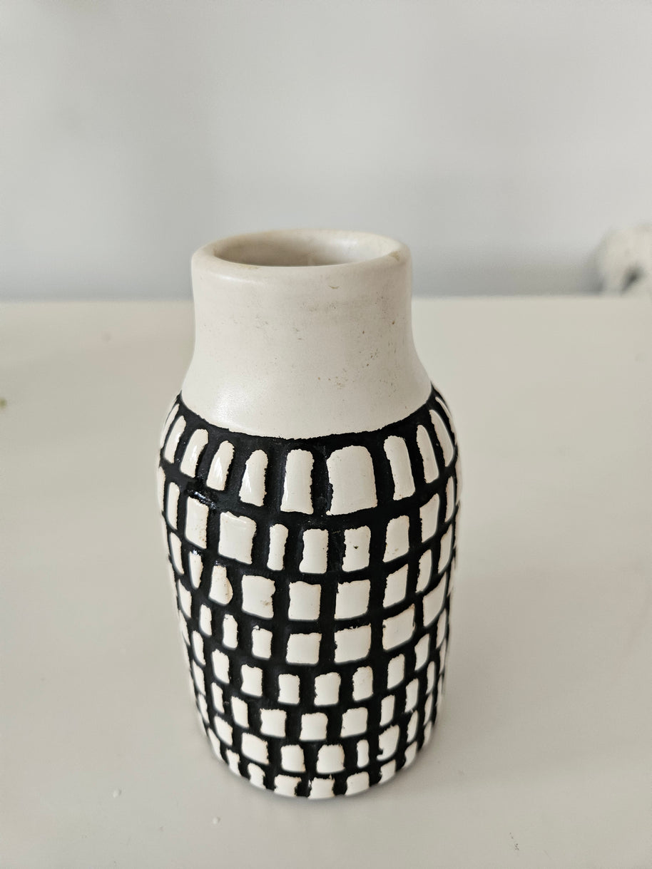 Cylindrical ceramic vase with black and white checkered pattern on a plain background