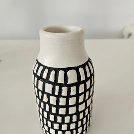 Cylindrical ceramic vase with black and white checkered pattern on a plain background