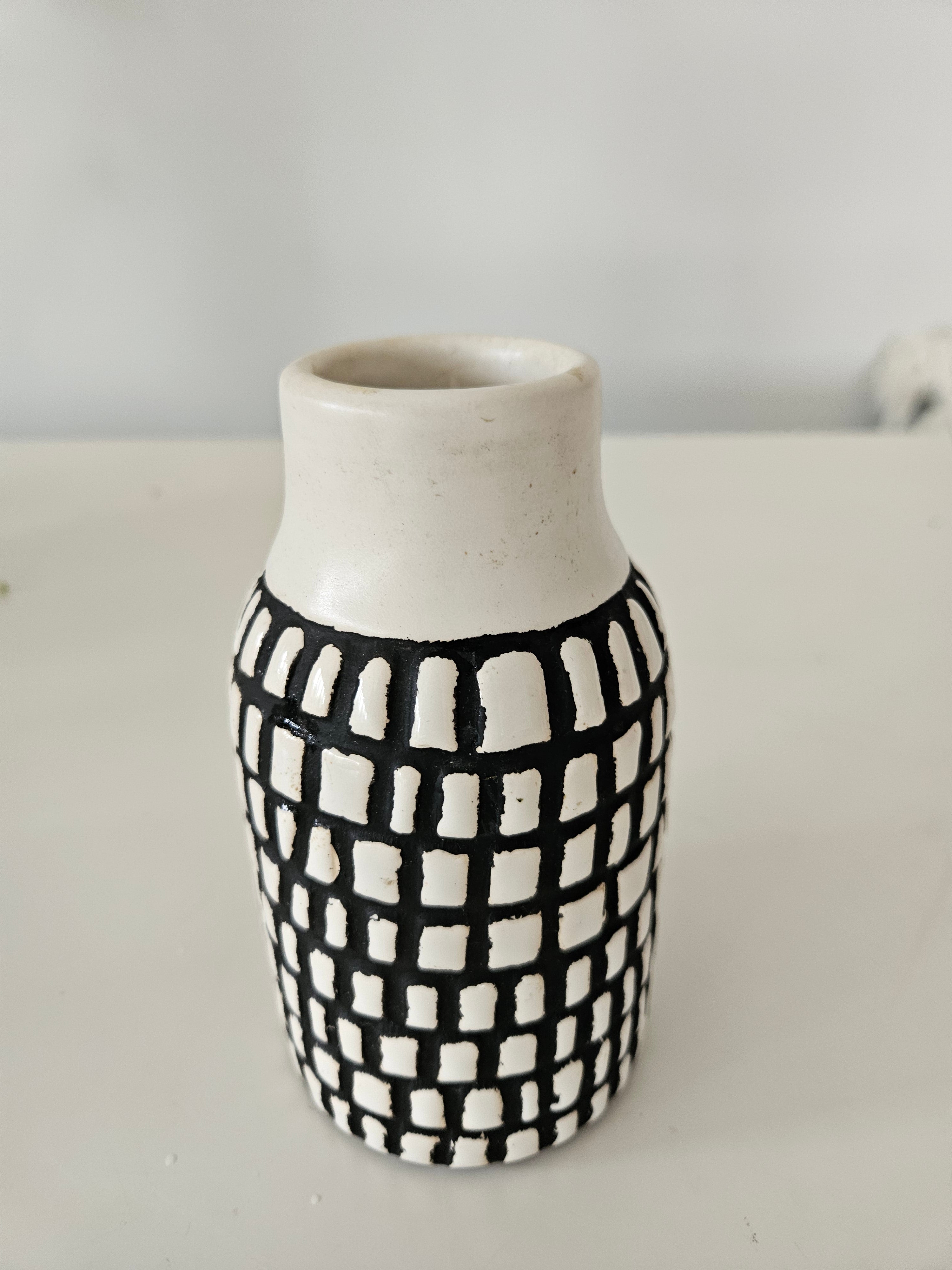 Cylindrical ceramic vase with black and white checkered pattern on a plain background