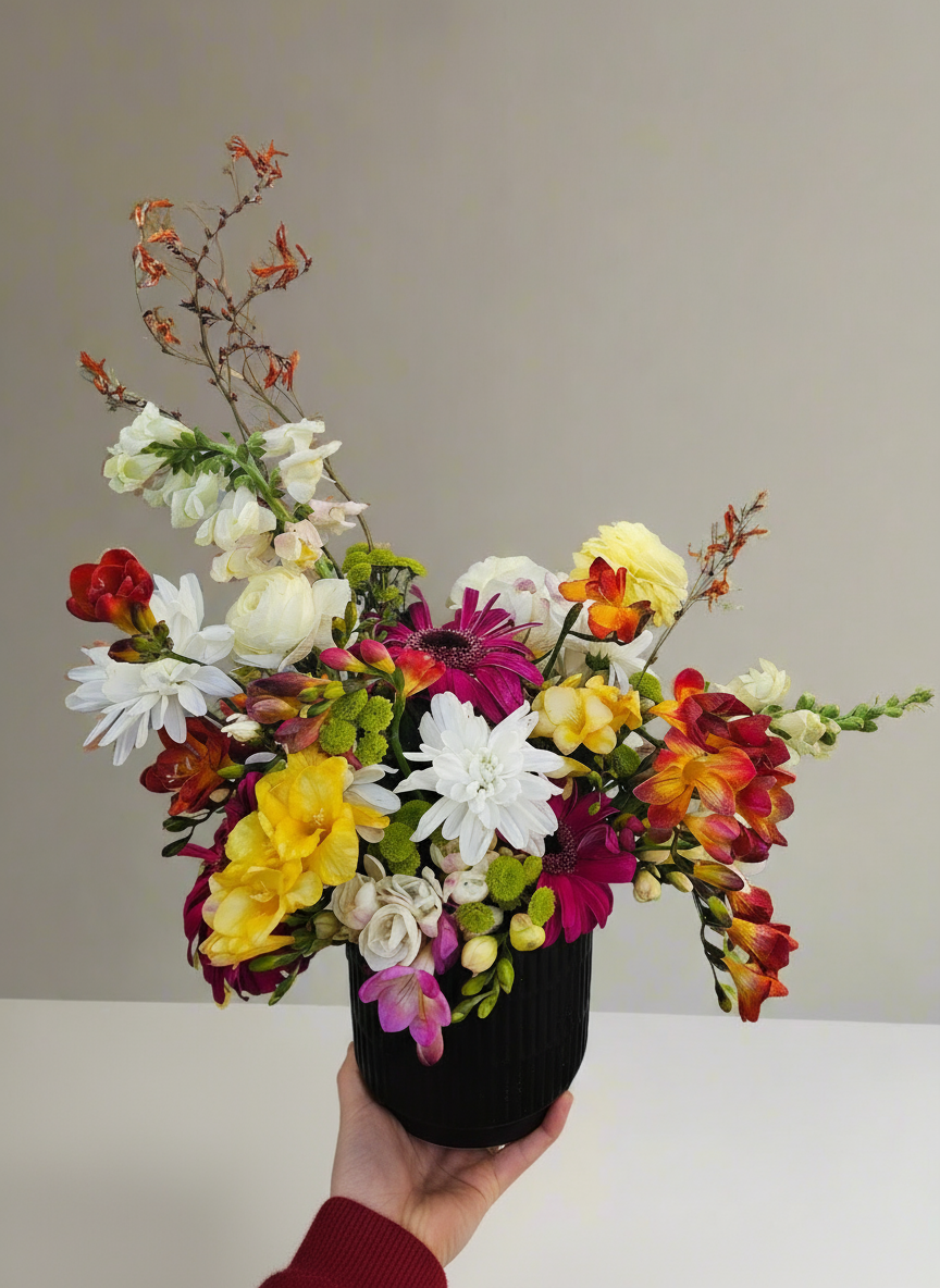 Colourful flower arrangement in a black vase held against a neutral background