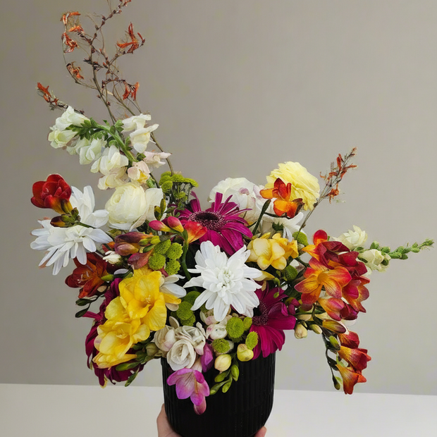 Colourful flower arrangement in a black vase held against a neutral background