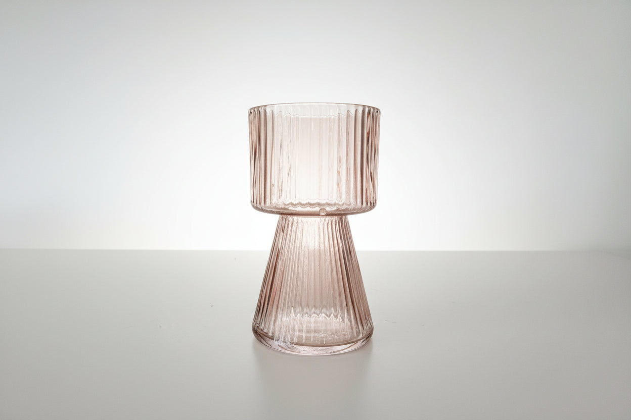 Side view of a peach pink ribbed glass vase on a white background