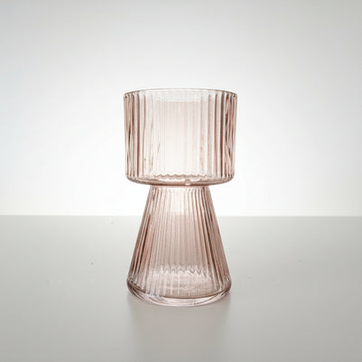 Side view of a peach pink ribbed glass vase on a white background