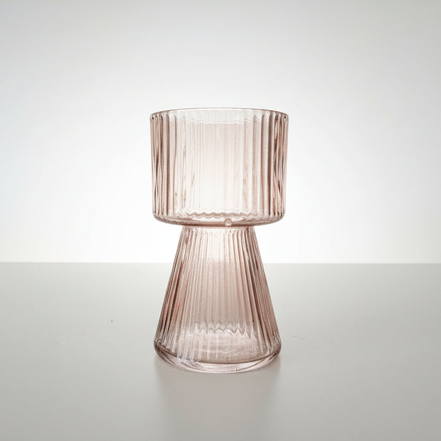 Side view of a peach pink ribbed glass vase on a white background