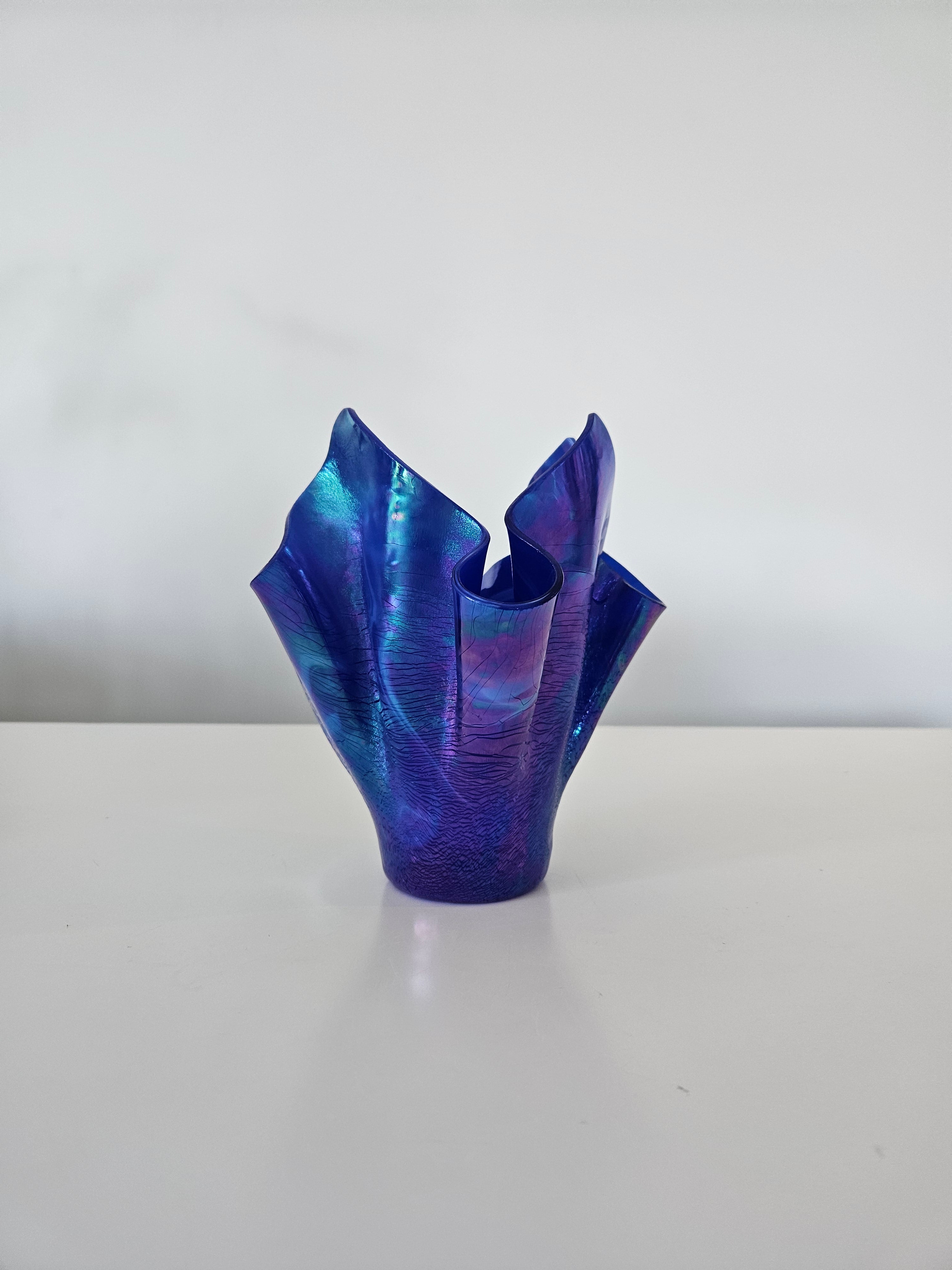 Side view of a blue and purple handkerchief style glass vase on a white background
