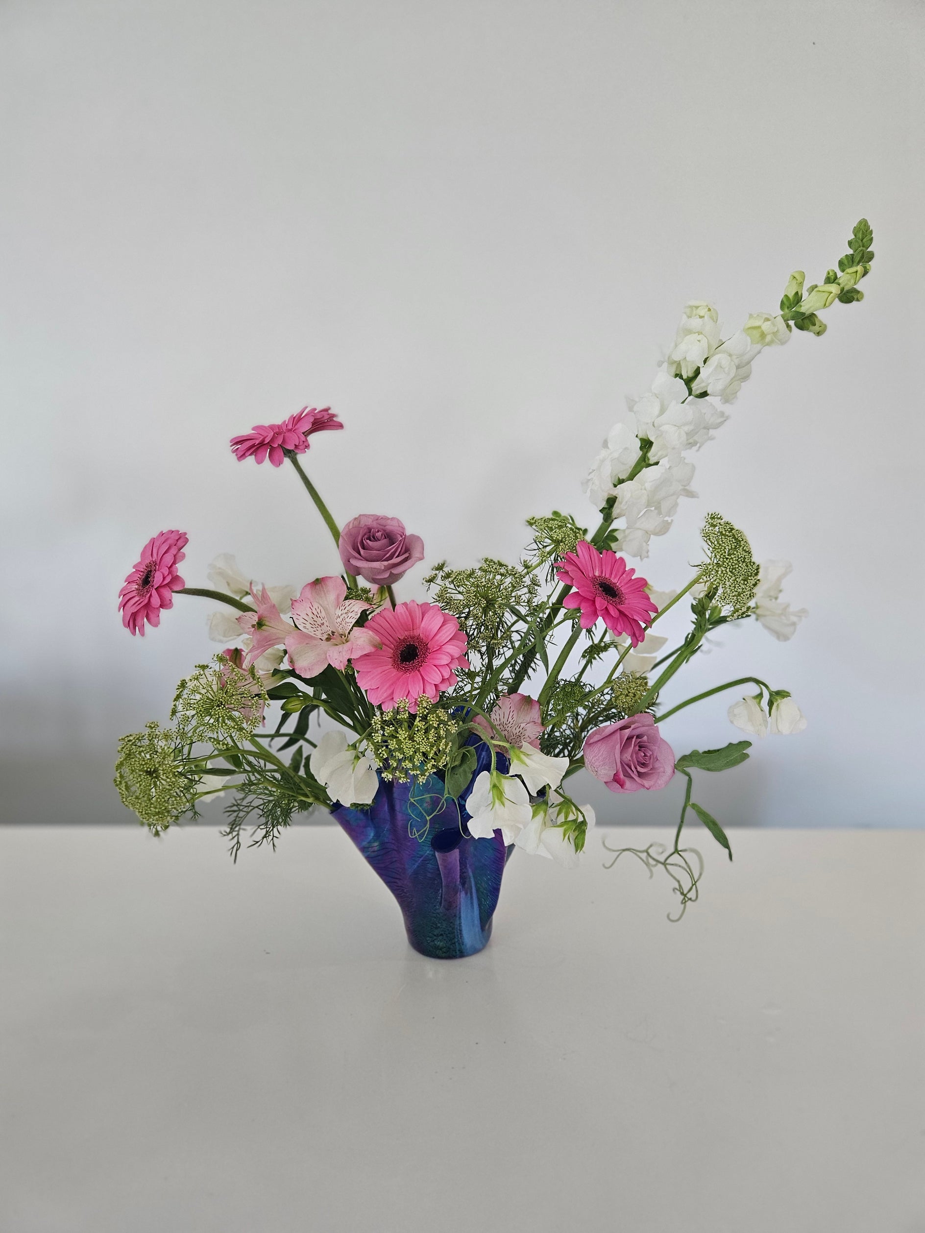 Floral arrangement with pink and white flowers in a blue vase against a white background
