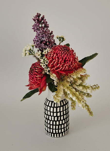 Floral arrangement in a black and white patterned vase on a gray background