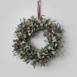 Dried flowers and eucalyptus Christmas wreath with a crimson ribbon on a plain background